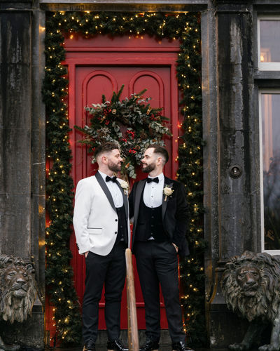 Newlywed grooms standing beside Christmas Wreath at Castle Wedding Venue