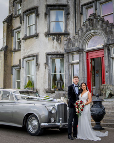 Newlywed couple pose with vintage car at irish castle hotel wedding