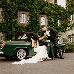 Bride and groom existing their vintage car at castle wedding venue