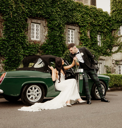 Bride and groom existing their vintage car at castle wedding venue